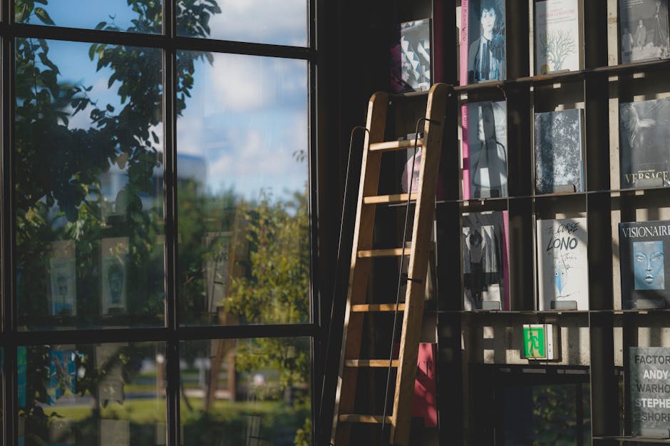 A wooden ladder leaning against a bookshelf in a sunlit library near a window.